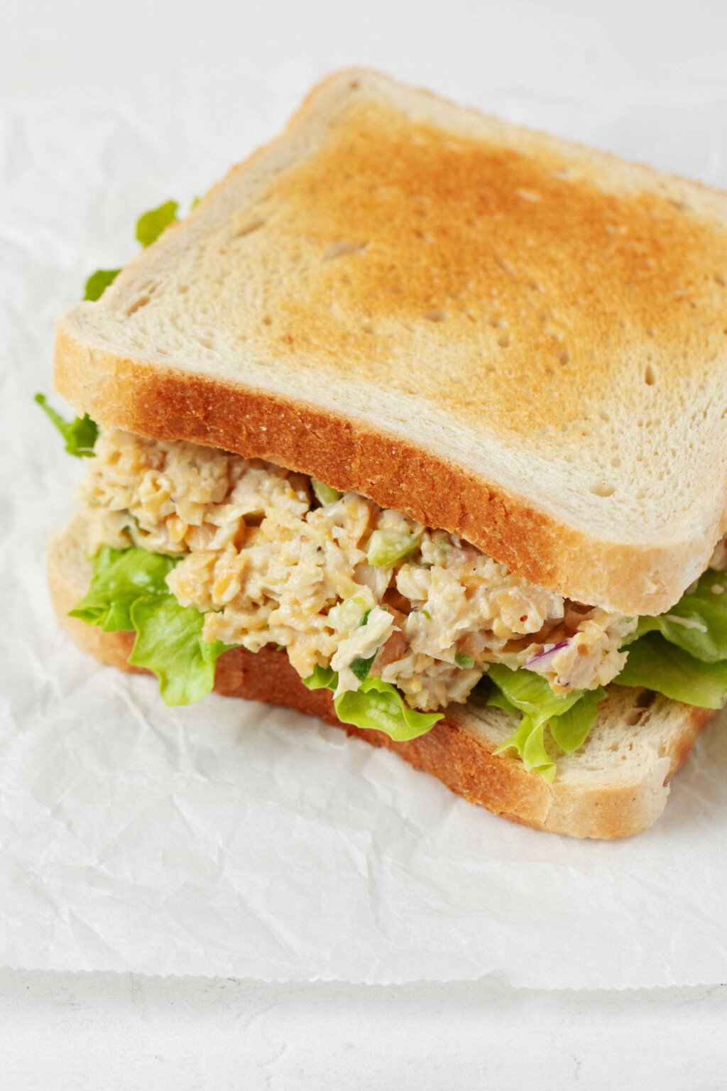Two slices of white sandwich bread have been piled high with artichoke heart and chickpea-based vegan tuna salad.