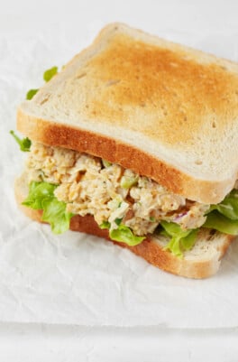 Two slices of white sandwich bread have been piled high with artichoke heart and chickpea-based vegan tuna salad.