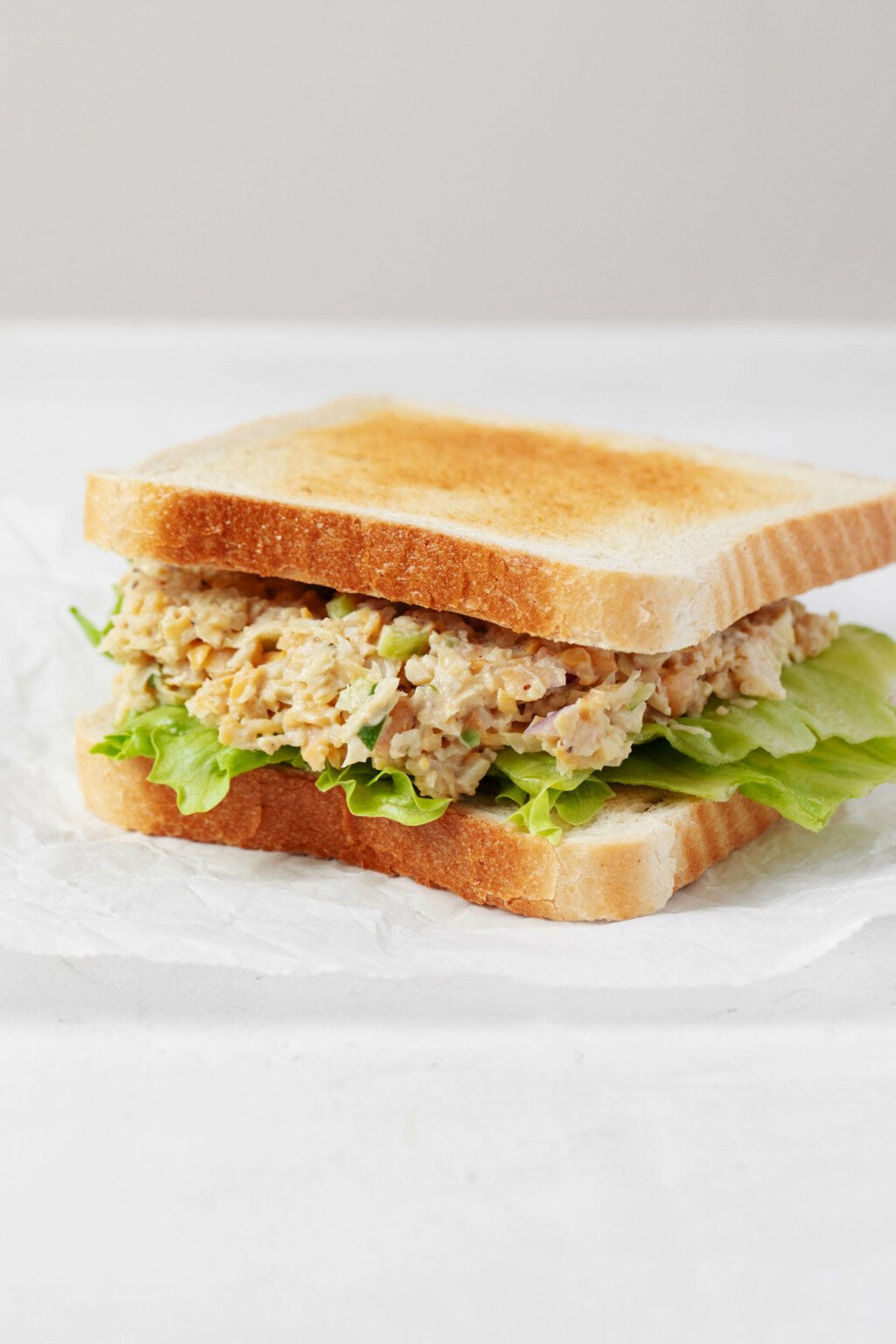 Two slices of white sandwich bread have been piled high with artichoke heart and chickpea-based vegan tuna salad.