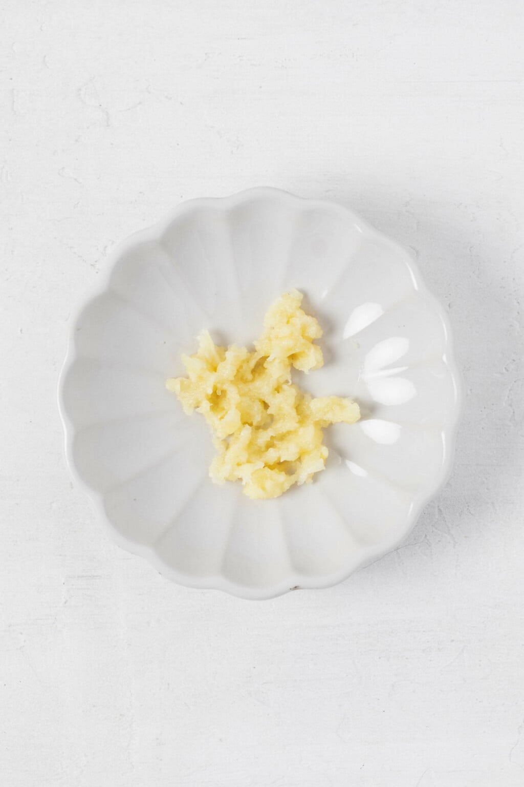 An overhead image of a small, fluted pinch bowl, filled with minced garlic.