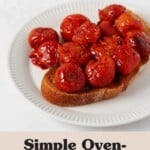 A slice of roasted bread has been piled high with red, oven-roasted cherry tomatoes. The bread is arranged on a round, fluted white plate.