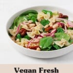 A round, white ceramic shallow bowl has been filled with a fresh spinach pasta salad, made with fresh green leaves of baby spinach and red sun-dried tomatoes.