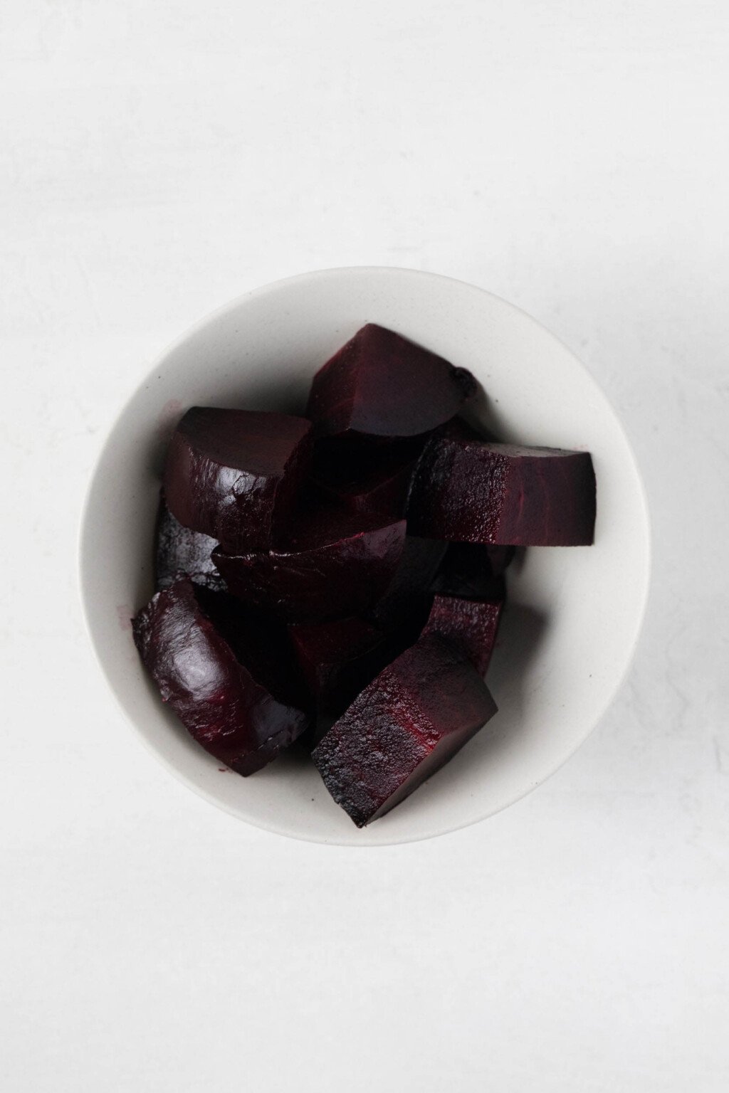 An overhead image of a small white bowl, which has been filled with cooked, roughly chopped beets. 