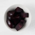 An overhead image of a small white bowl, which has been filled with cooked, roughly chopped beets.