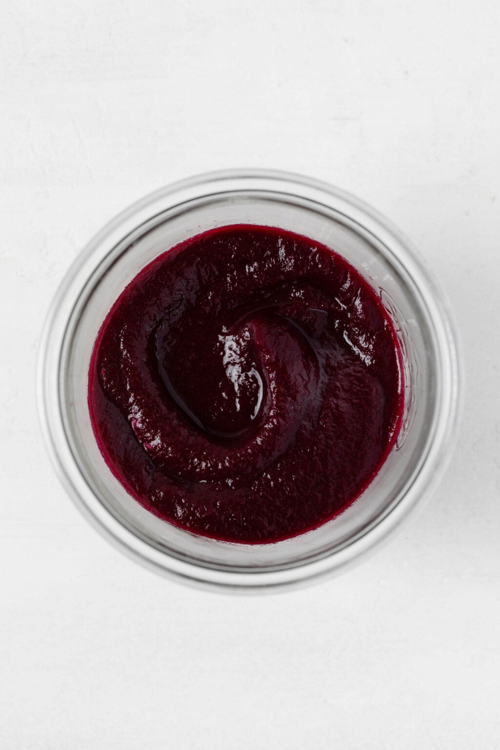 An overhead image of a glass mason jar, which is filled with a deep purple colored beet ketchup.