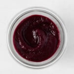 An overhead image of a glass mason jar, which is filled with a deep purple colored beet ketchup.