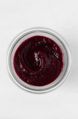 An overhead image of a glass mason jar, which is filled with a deep purple colored beet ketchup.