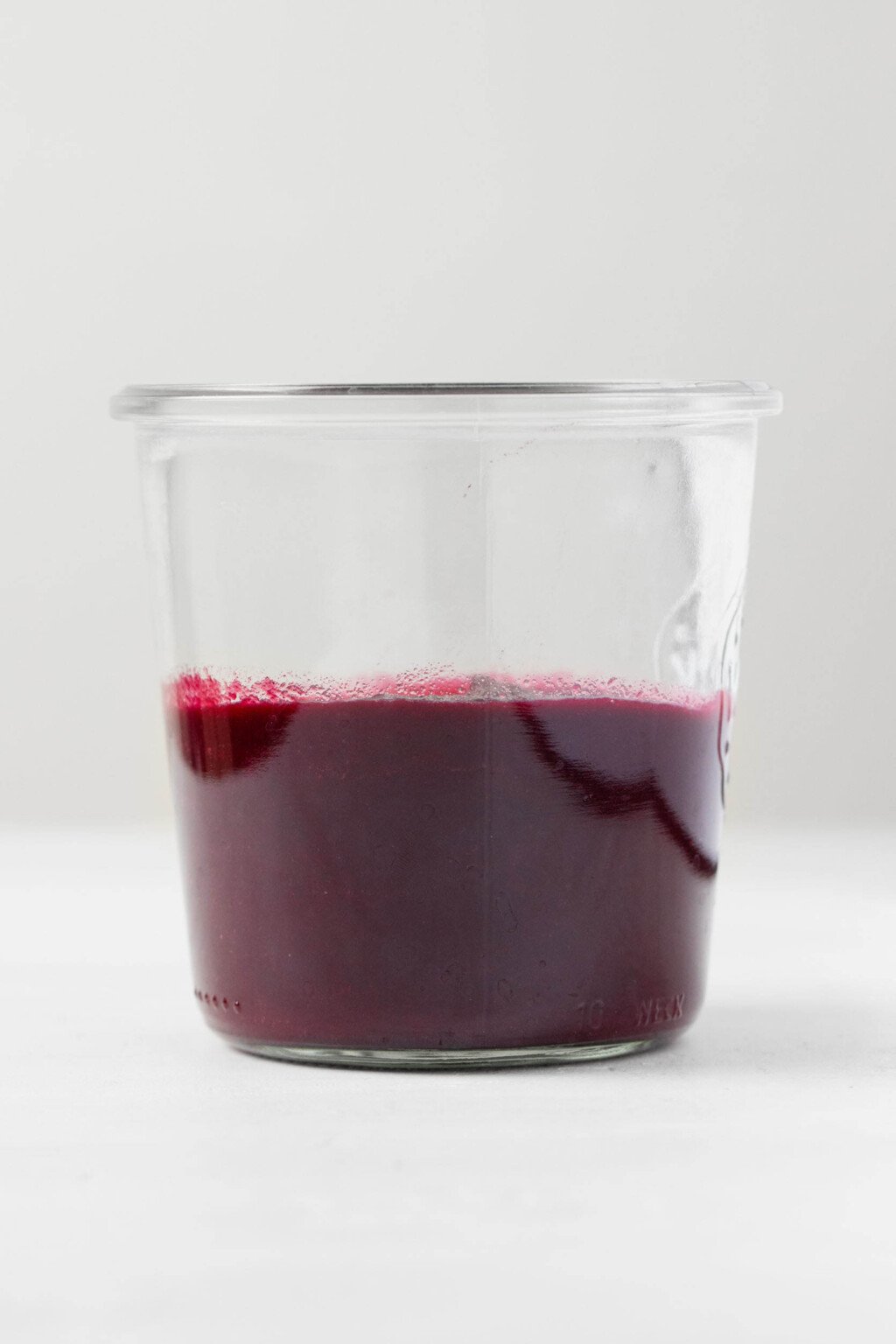 A sideways image of a glass mason jar, which is filled with a deep purple colored beet ketchup.