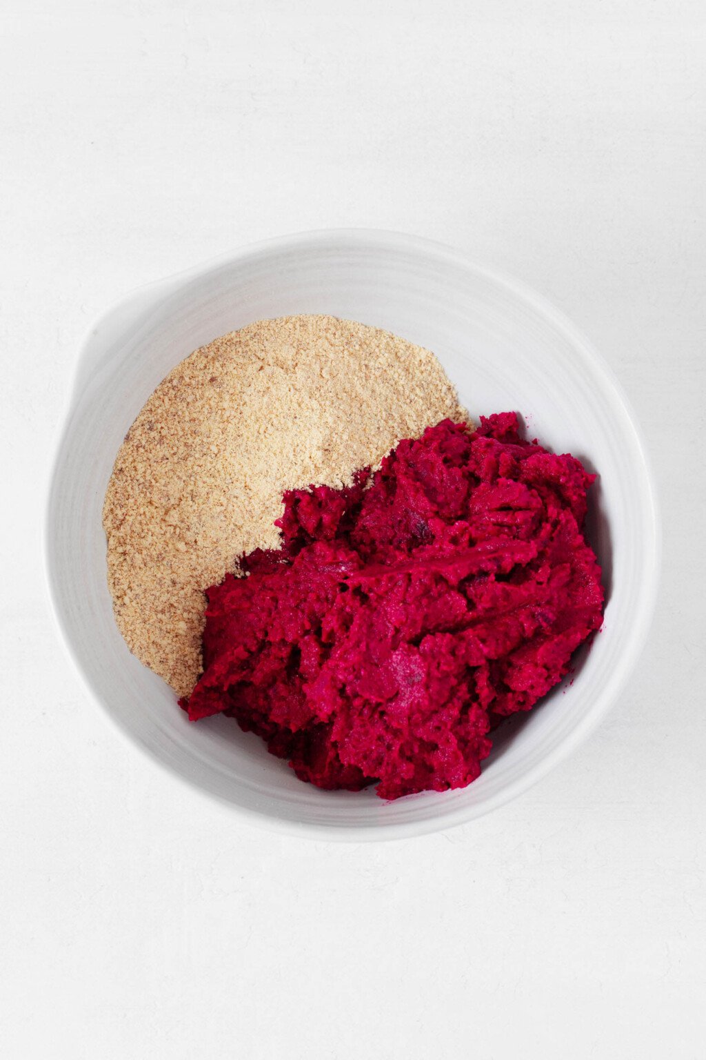 Puréed beets are pictured in a white mixing bowl along with ground almonds.