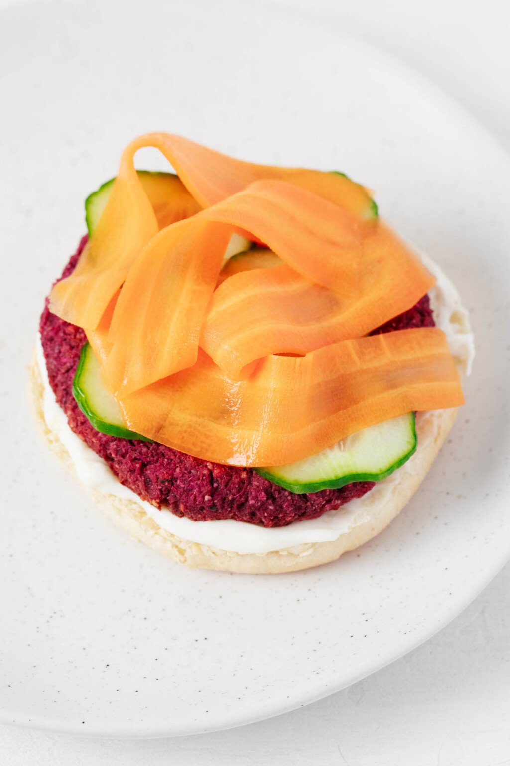 A vegan burger, made bright pink thanks to beets, is topped with cucumber slices and carrot "ribbons."