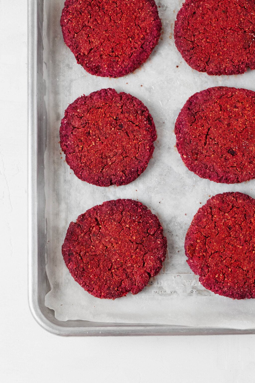 Bright pink vegan burgers, made with chickpeas and beets, have just been baked. They're pictured on a parchment-lined baking sheet.