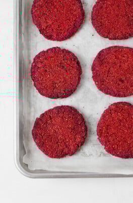 Bright pink vegan burgers, made with chickpeas and beets, have just been baked. They're pictured on a parchment-lined baking sheet.