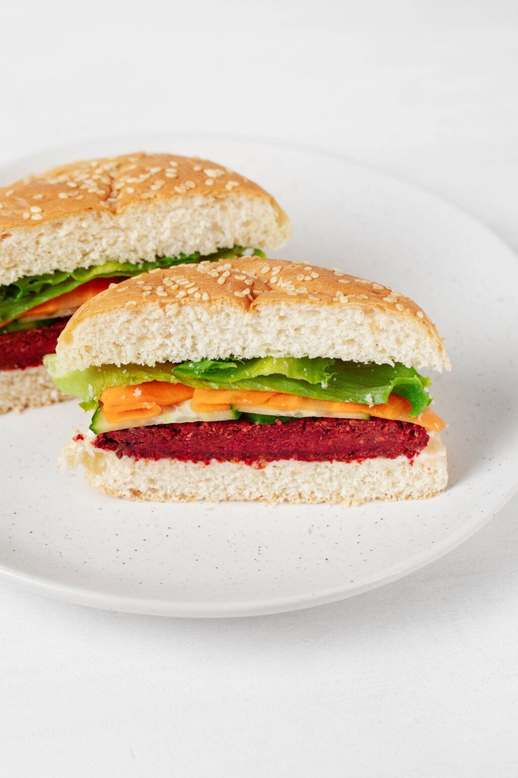 A vegan chickpea and beet burger has been served with fresh carrots and cucumber slices on a golden white burger bun.