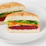 A vegan chickpea and beet burger has been served with fresh carrots and cucumber slices on a golden white burger bun.