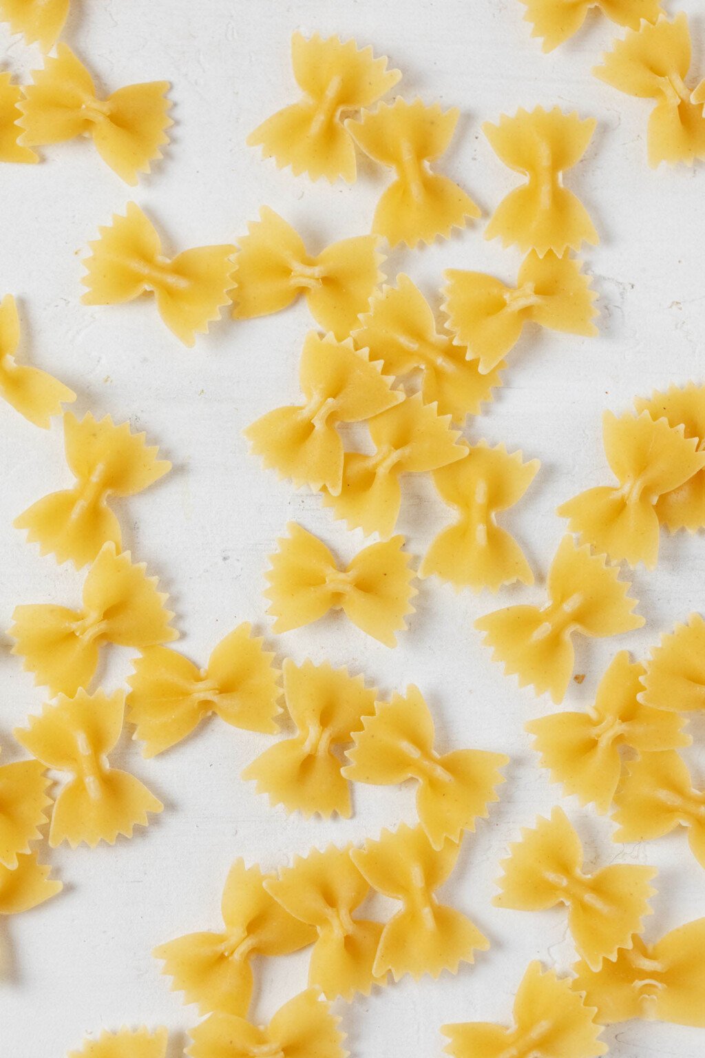 Dry farfalle pasta are arranged on a white surface.