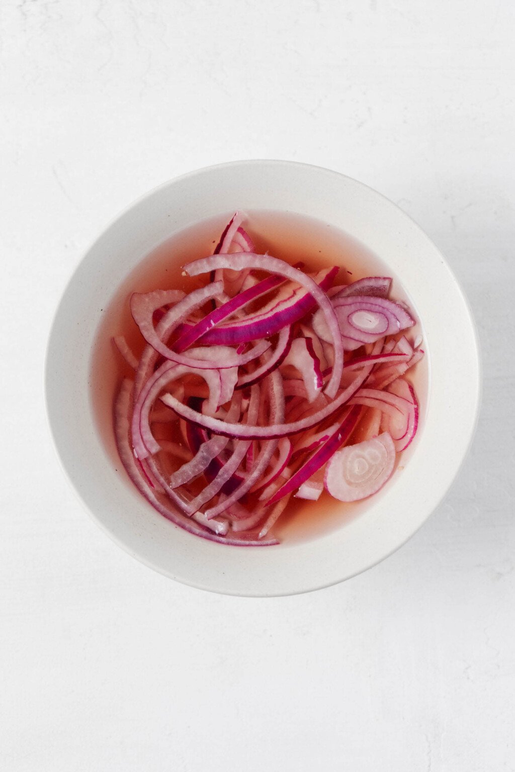 An overhead image of a small, white bowl, which holds pickled red onions.