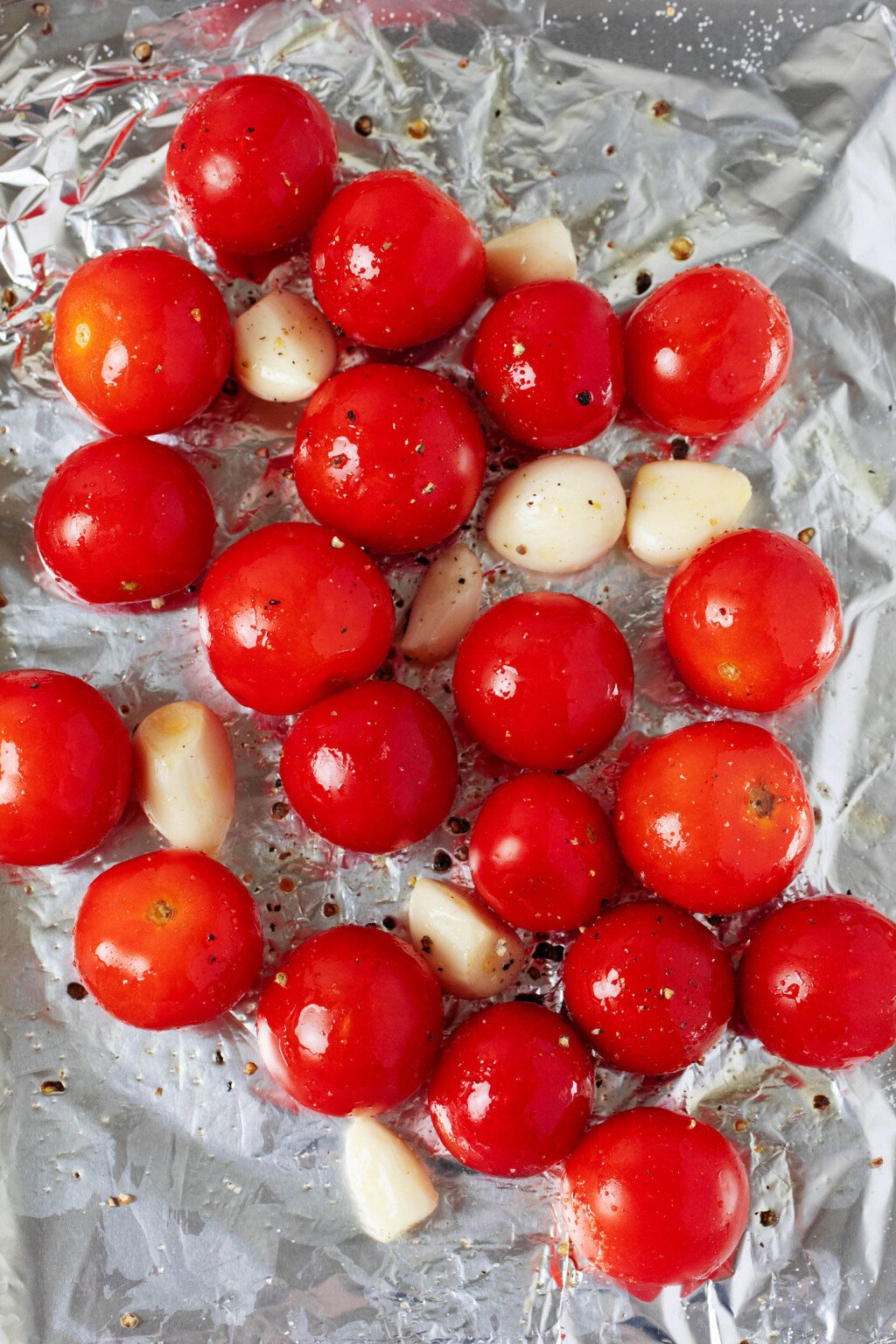 An overhead image of cherry tomatoes and garlic cloves that have been arranged on a foil-lined baking sheet.