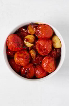 Roasted garlic cloves and vegetables have been piled into a round, small white bowl.