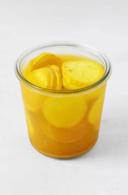 A clear Weck mason jar has been filled with pickled yellow squash slices.