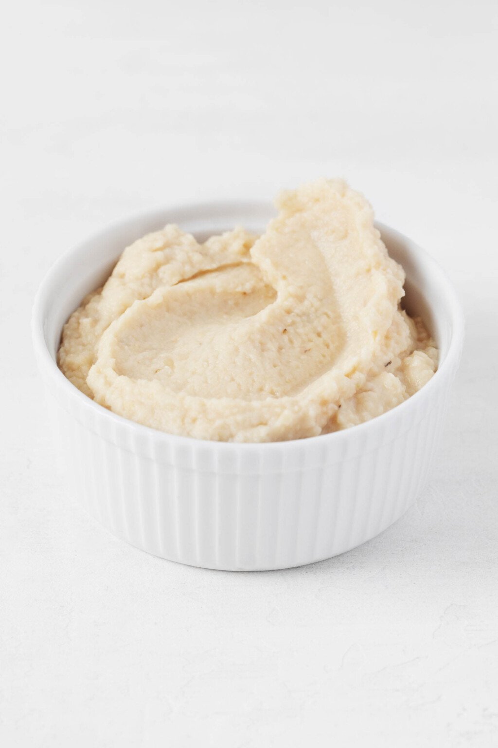 A creamy vegan white bean dip has been piled into a small white bowl.