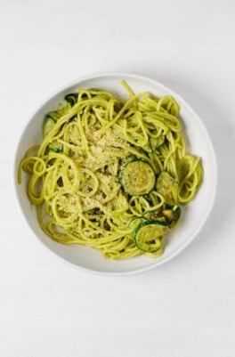 An overhead image of a white bowl of vegan zucchini pasta, prepared with spaghetti and with slices of pan-fried zuchini.