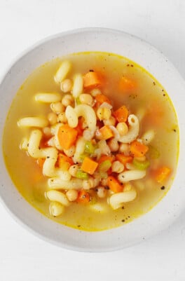 An overhead image of a round, white ceramic bowl, which is filled with a vegan chickpea noodle soup.