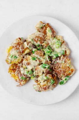 An overhead image of a vegan crispy smashed potato salad, served on a simple round white plate.