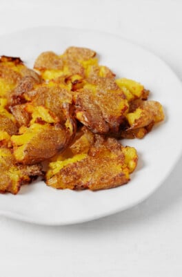 Browning, crispy vegan smashed potatoes are served in a shallow white dish.