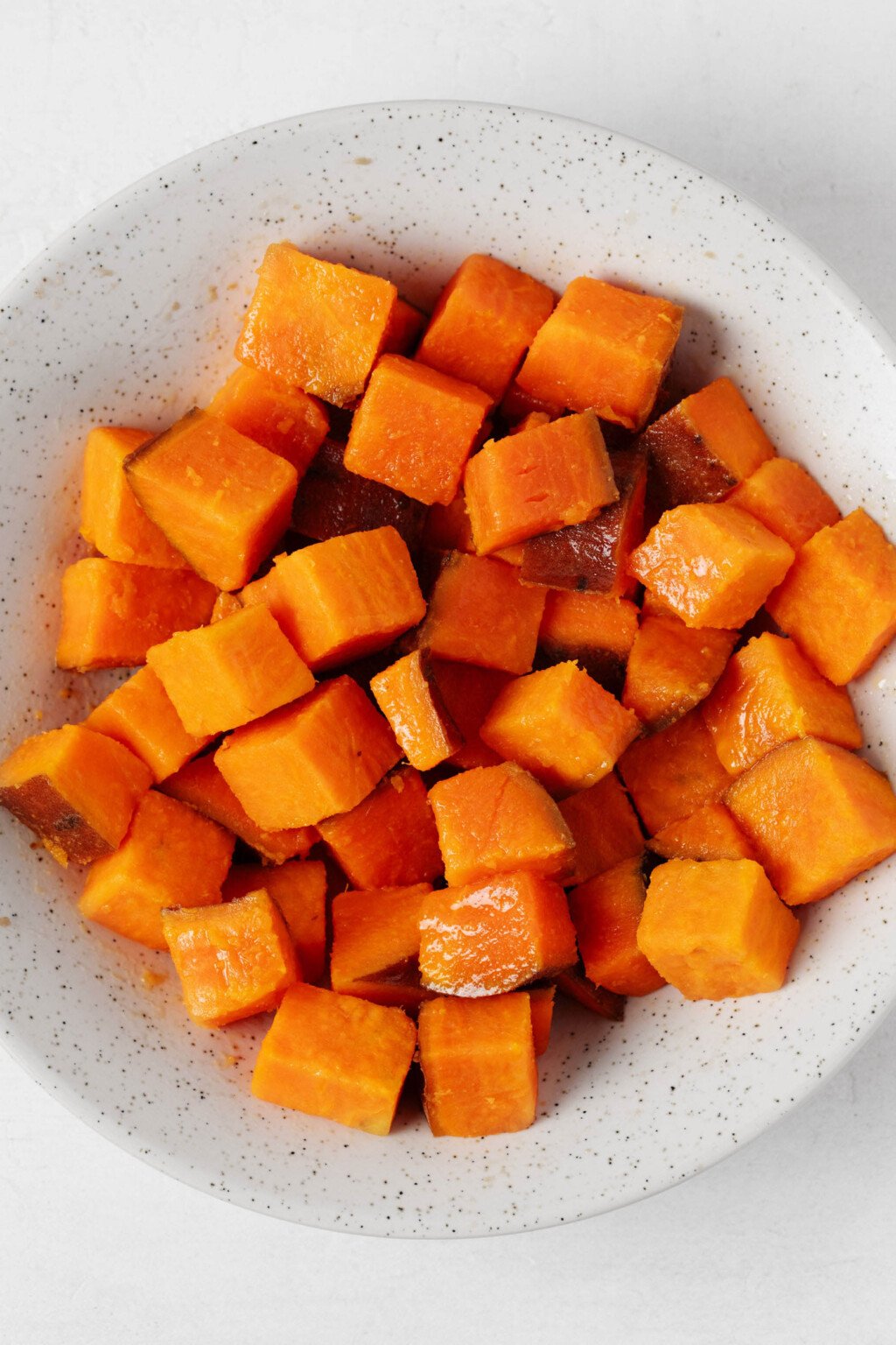 The white bowl holds three-dimensional cooked pieces of orange sweet potato.