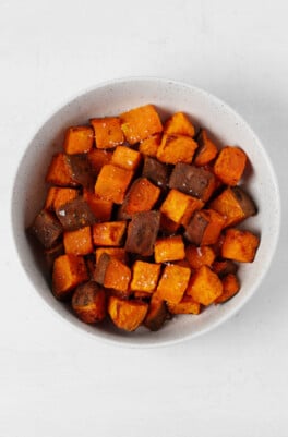 A white bowl contains cubed, deep orange air fryer sweet potatoes, which are seasoned with salt and pepper.