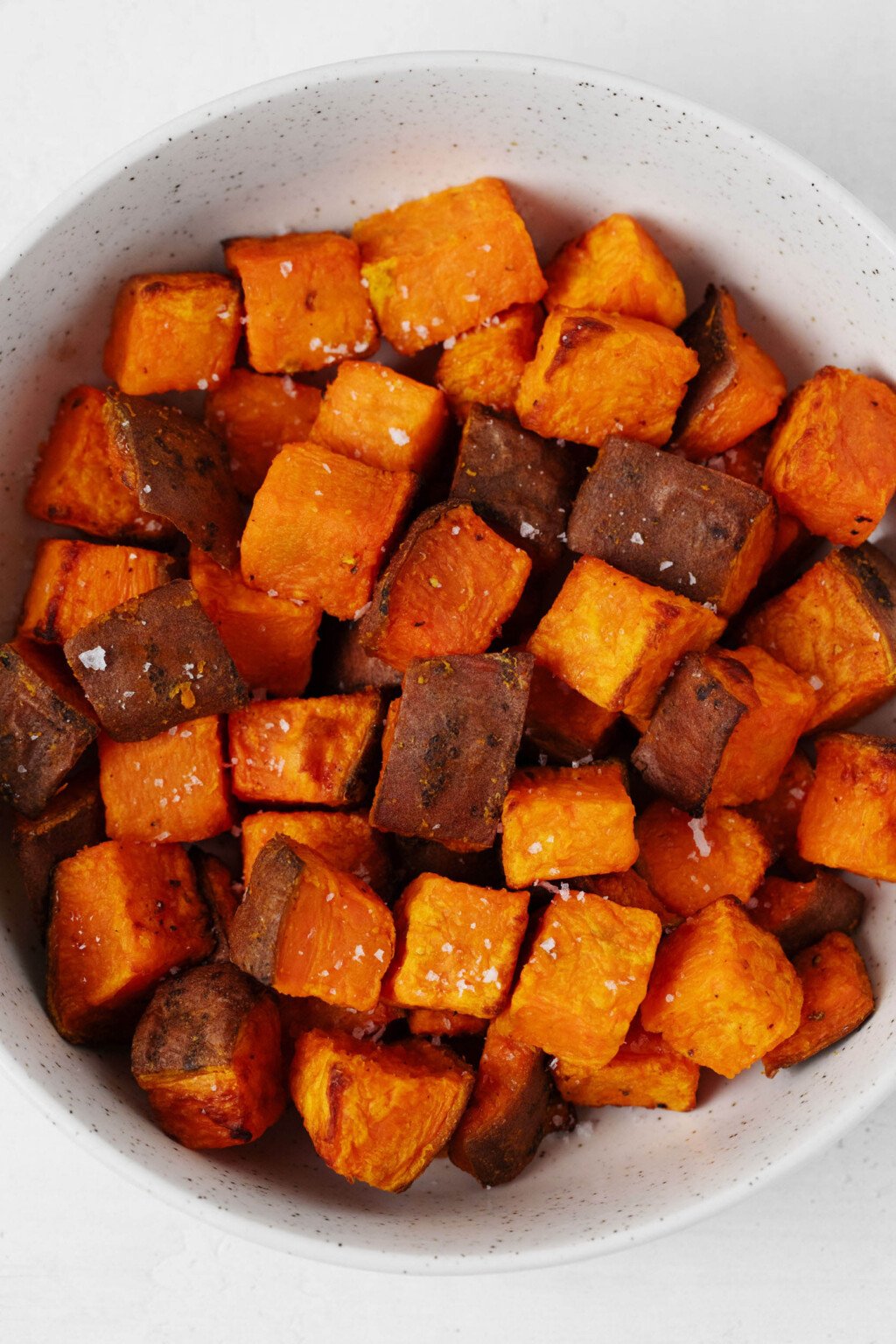 The white bowl contains a thick orange air fryer sweet potato, seasoned with salt and pepper.