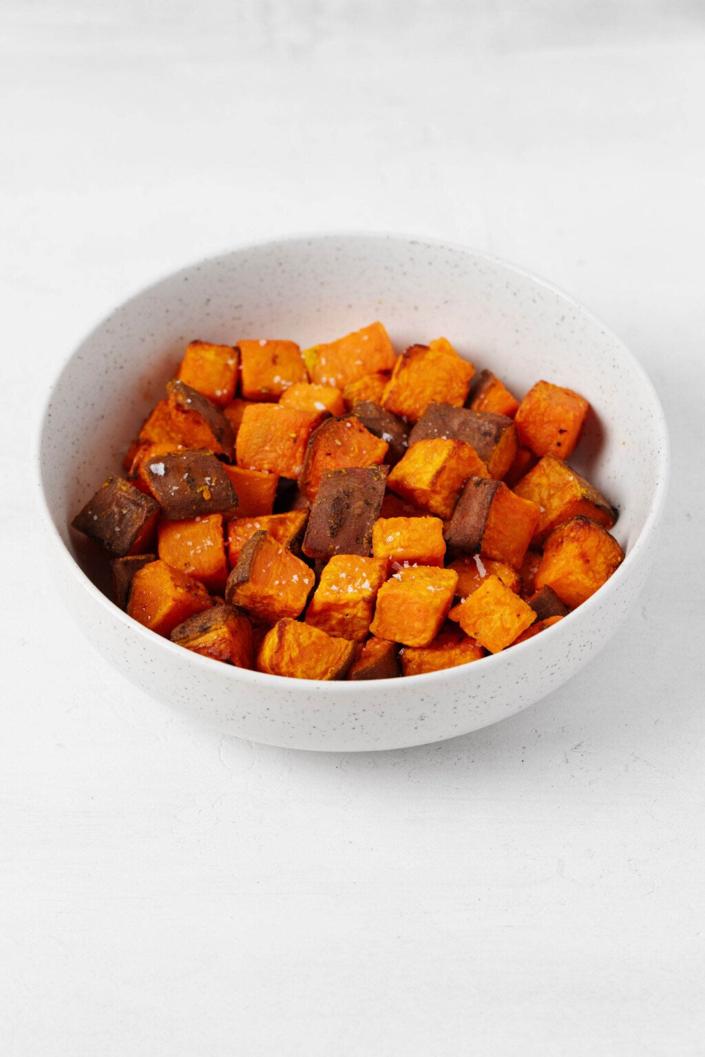 The white bowl contains a thick orange air fryer sweet potato, seasoned with salt and pepper.