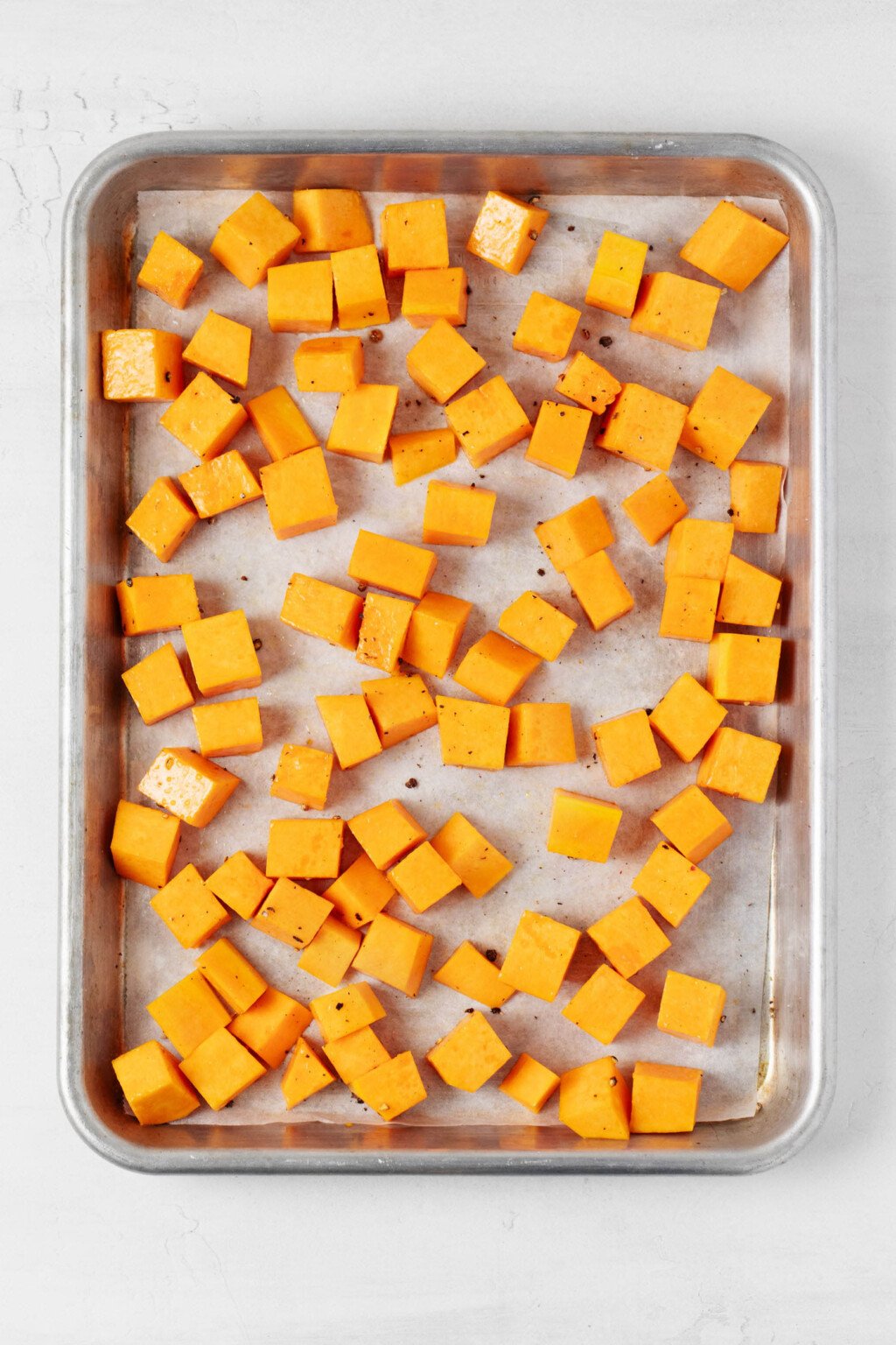 Cubed pieces of butternut squash are arranged on a metal sheet pan. 