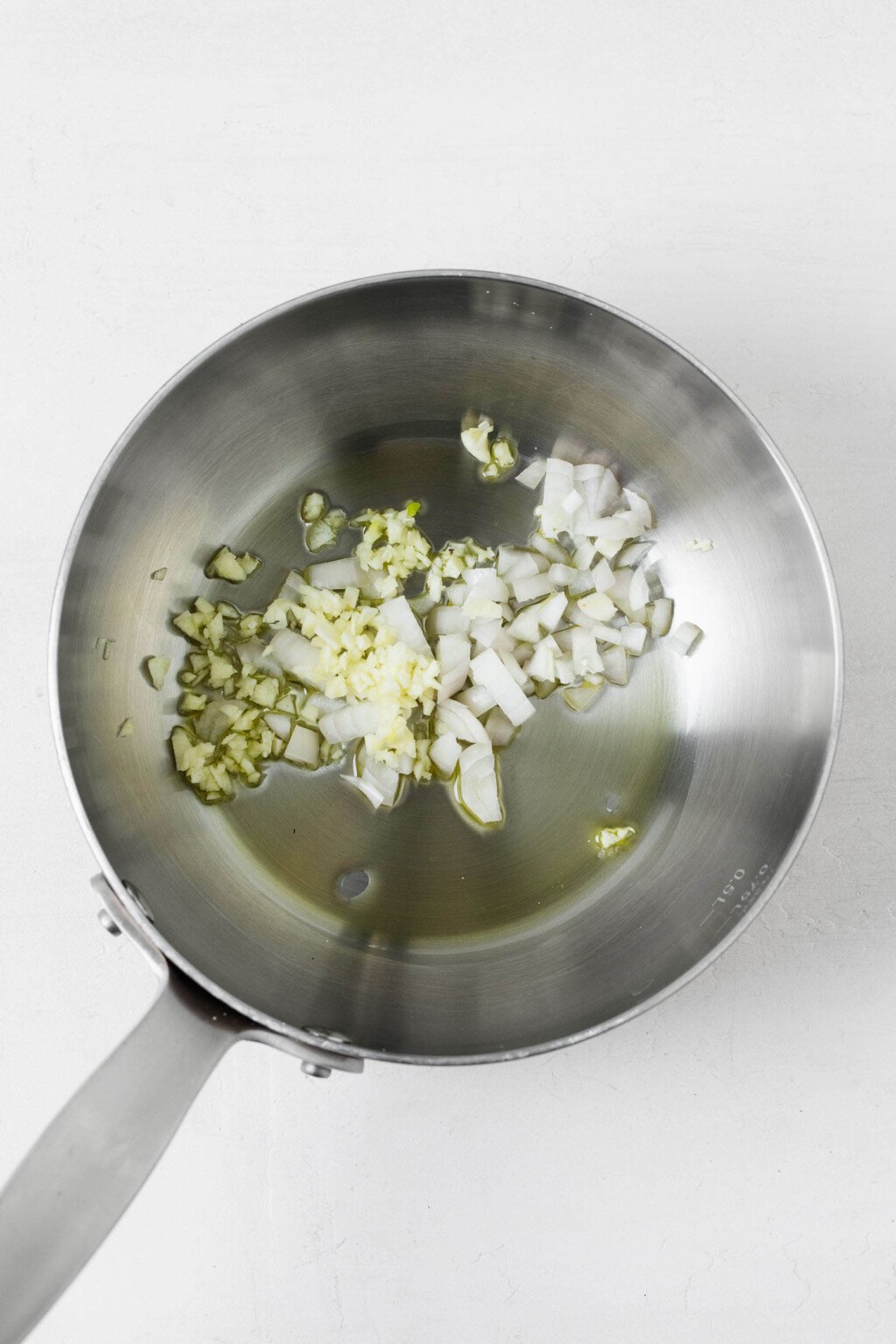 Garlic and shallot are being sautéed in a small stainless steel frying pan.