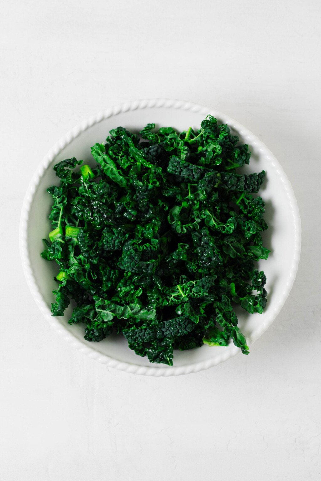 An overhead image of a white ceramic bowl, which has been filled to the brim with kale.