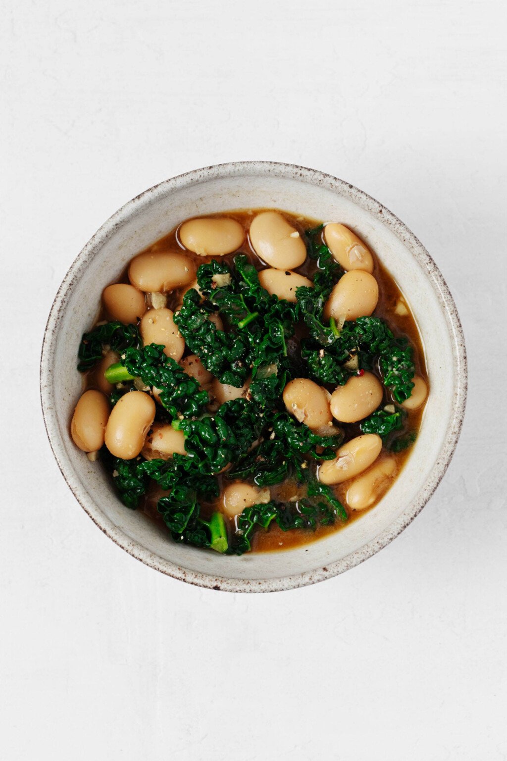 A brothy mixture of butter beans and greens is pictured in a bowl.