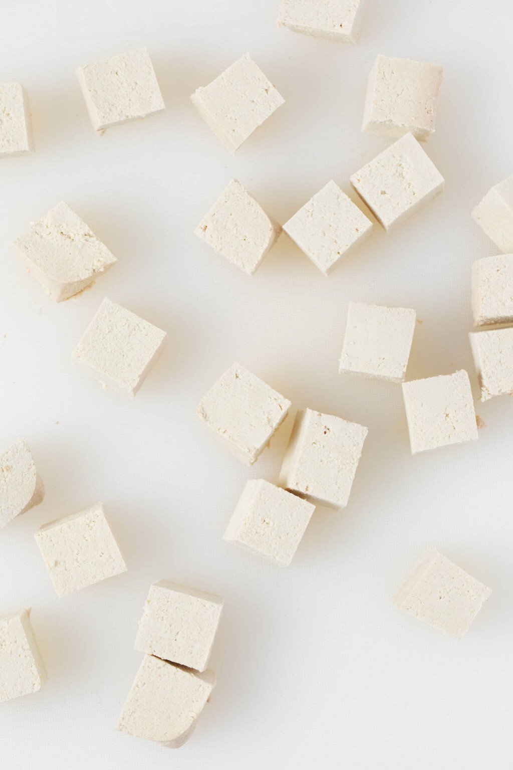 Cubed pieces of firm tofu rest on a bright white surface.