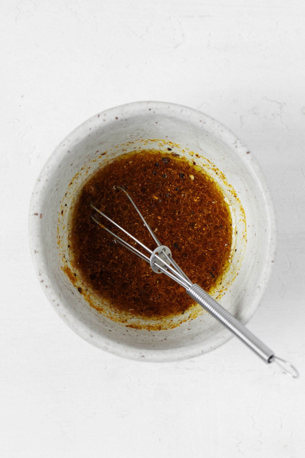 A marinade with curry powder, oil, and lemon juice is being whisked together in a small white ceramic bowl.