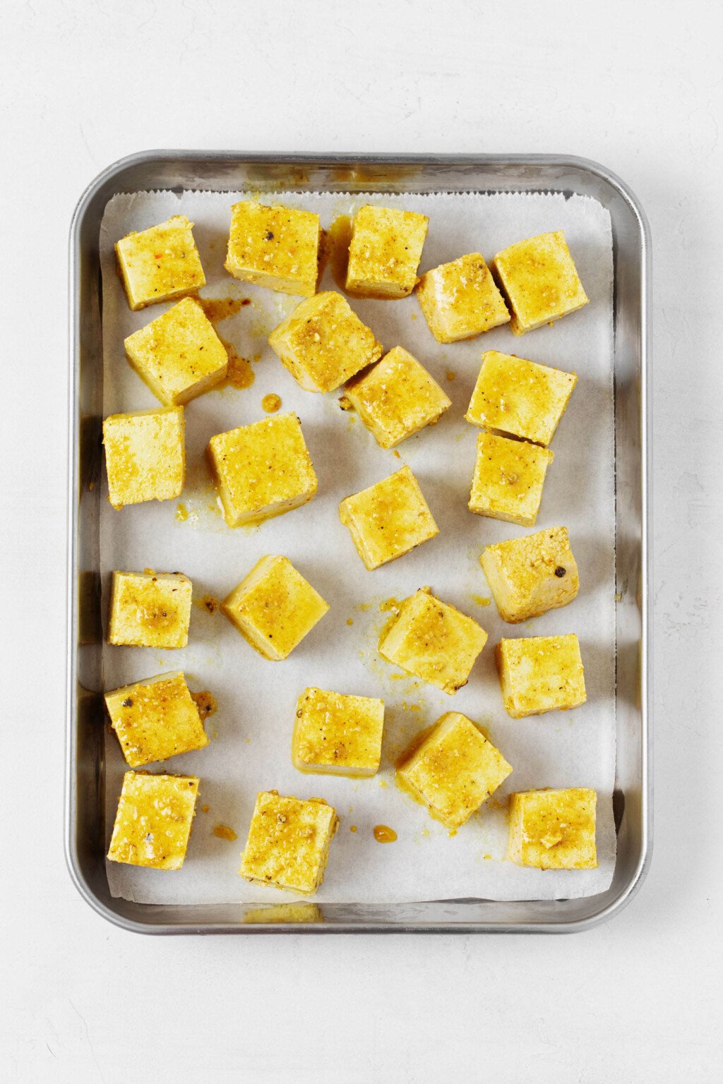 Golden colored curried tofu cubes rest on a parchment lined baking sheet.