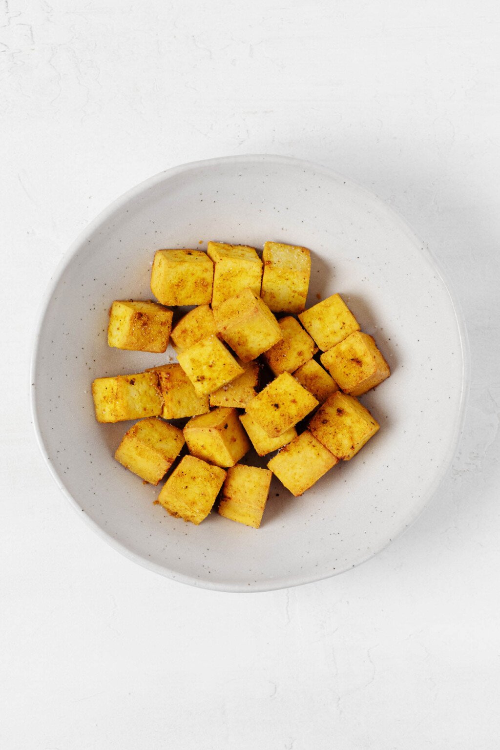 A round, wide-rimmed white bowl holds bright golden baked curried tofu cubes.
