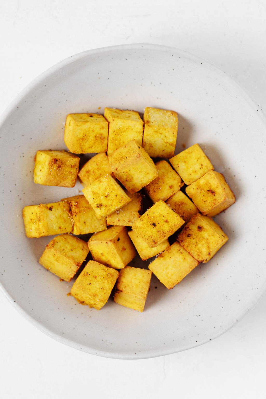 A round, wide-rimmed white bowl holds bright golden baked curried tofu cubes.