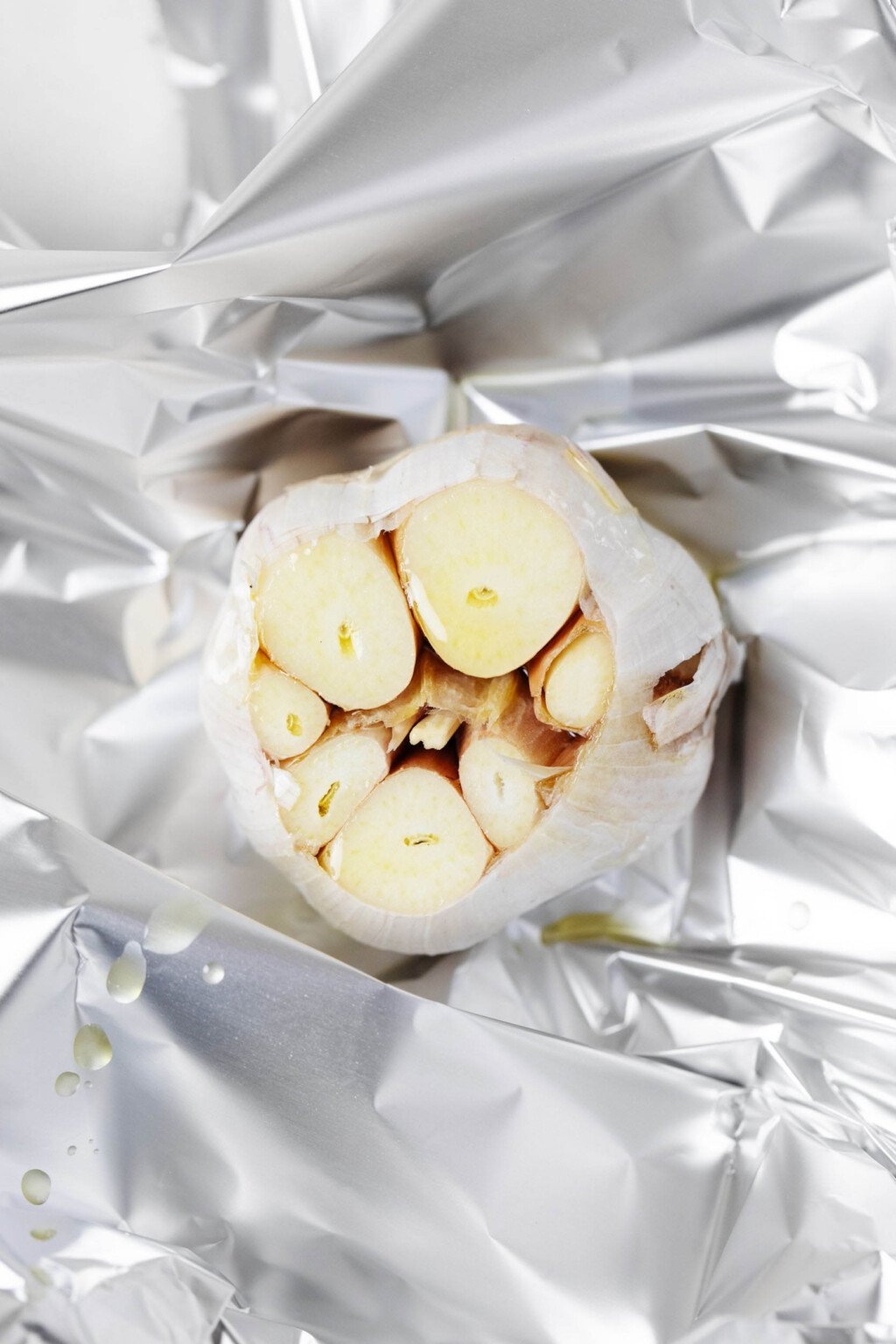 A bulb of garlic with its top sliced off crosswise is pictured on top of a sheet of foil.