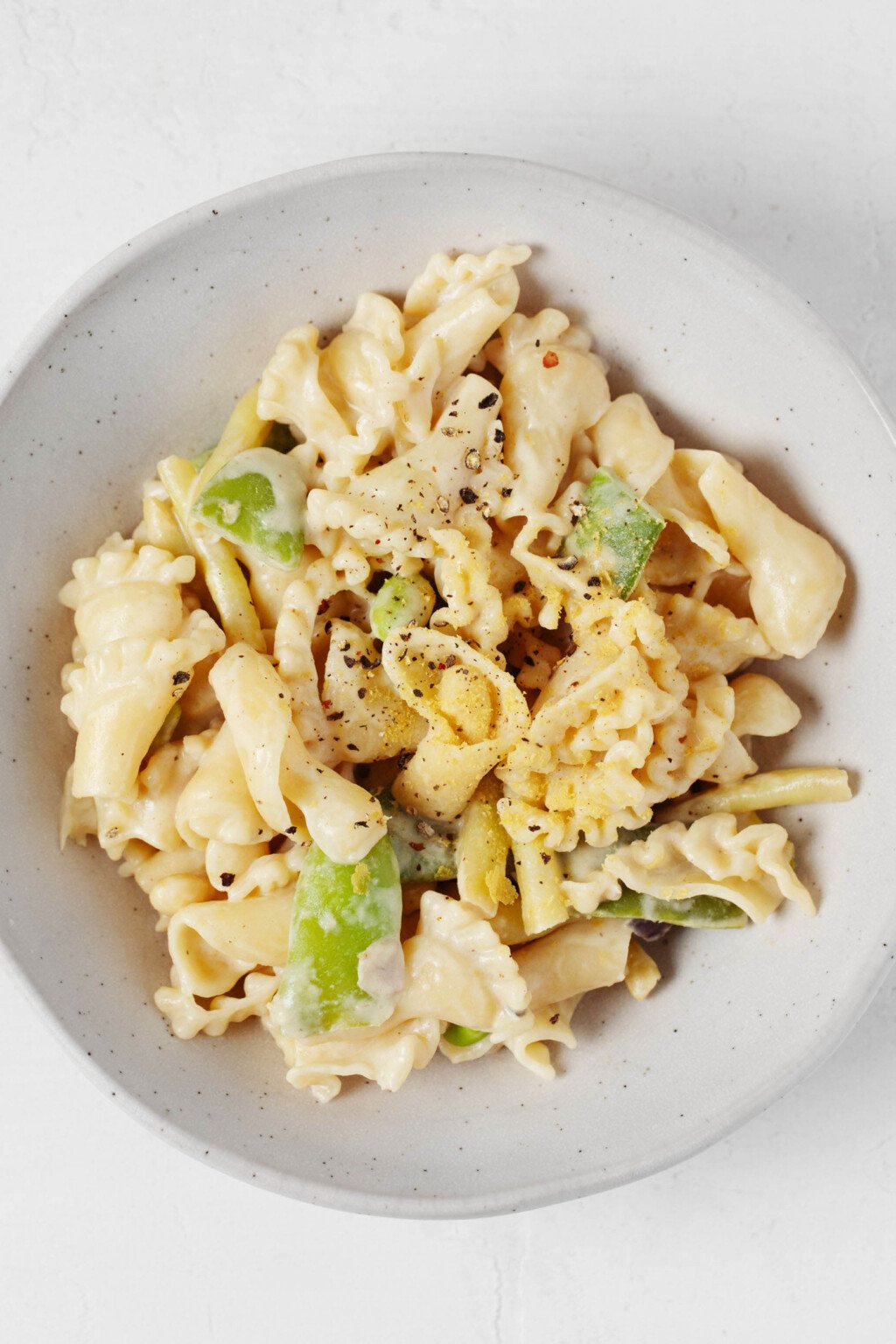 A roasted garlic tahini sauce has been used to make a light, creamy vegan pasta. It's served in a low, round white bowl.