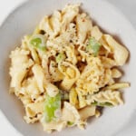 A roasted garlic tahini sauce has been used to make a light, creamy vegan pasta. It's served in a low, round white bowl.