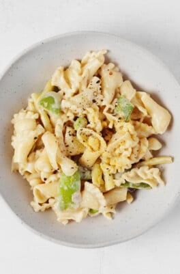 A roasted garlic tahini sauce has been used to make a light, creamy vegan pasta. It's served in a low, round white bowl.