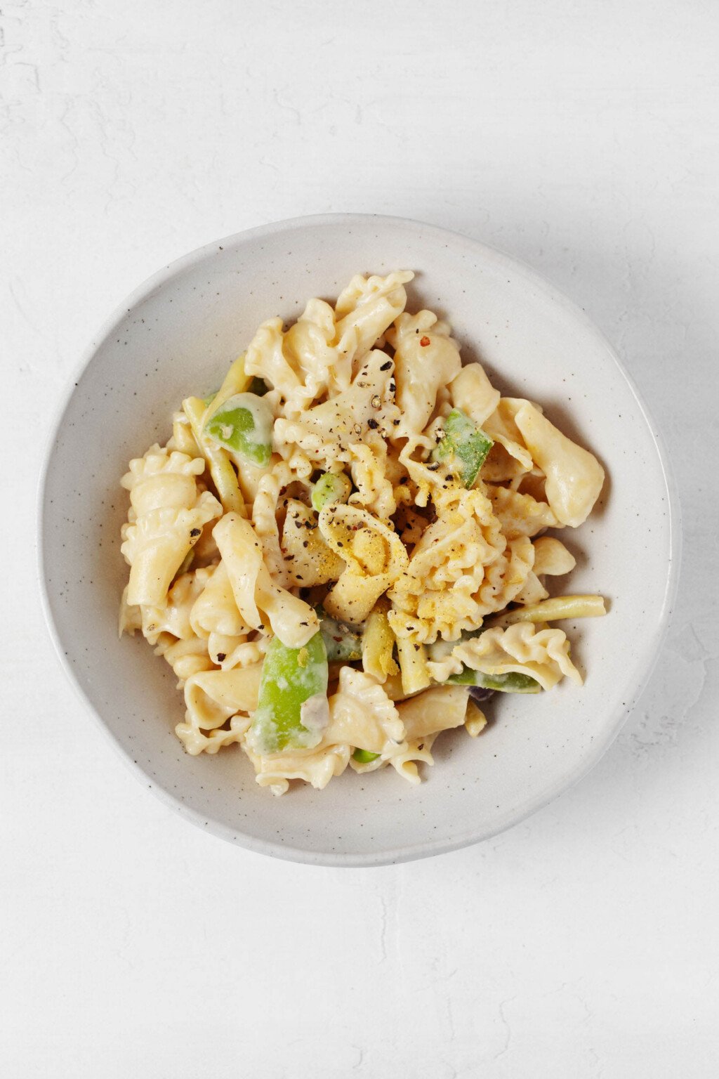 A roasted garlic tahini sauce has been used to make a light, creamy vegan pasta. It's served in a low, round white bowl.