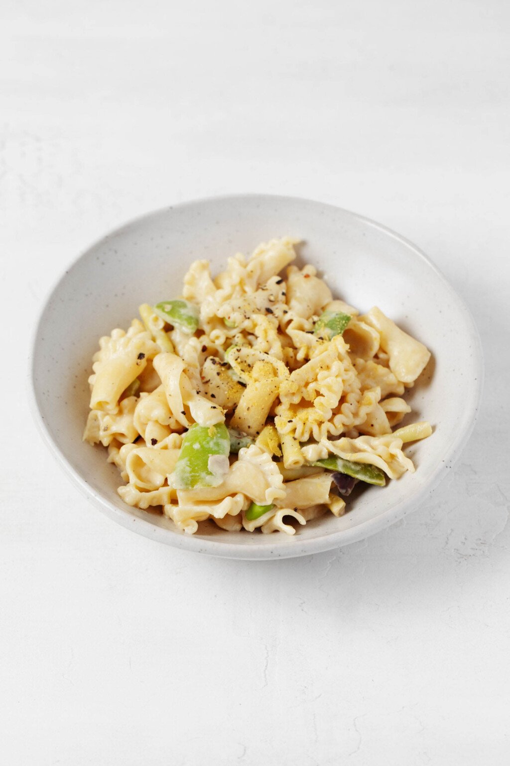 A roasted garlic tahini sauce has been used to make a light, creamy vegan pasta. It's served in a low, round white bowl.