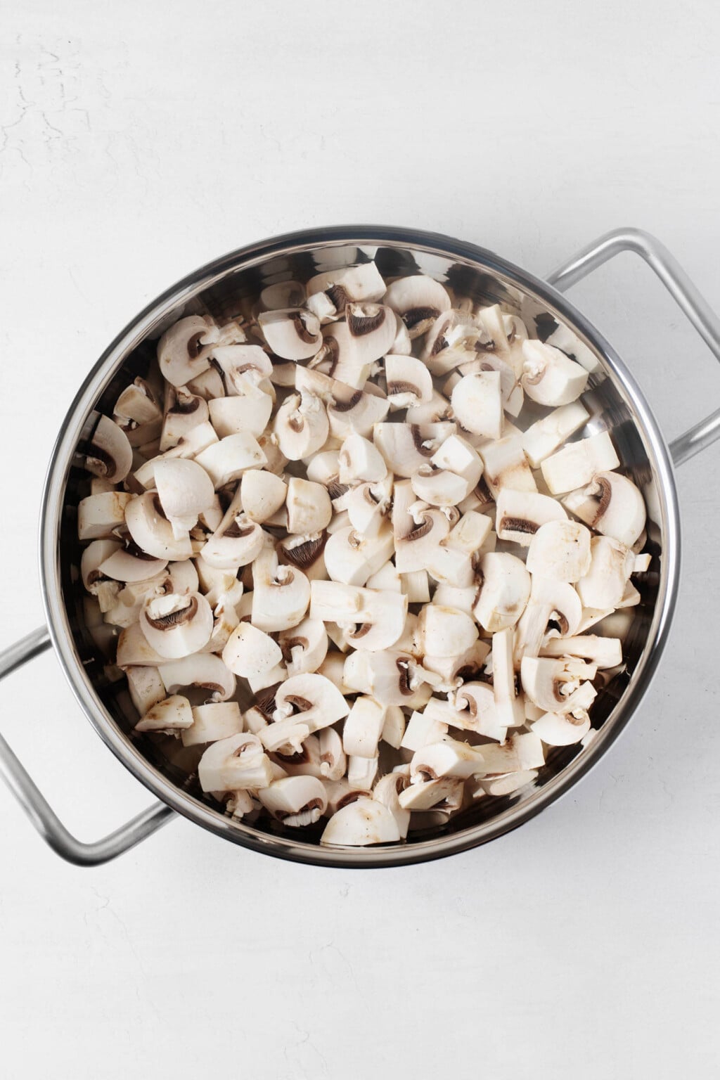 A large pot is full of raw, halved button mushrooms.