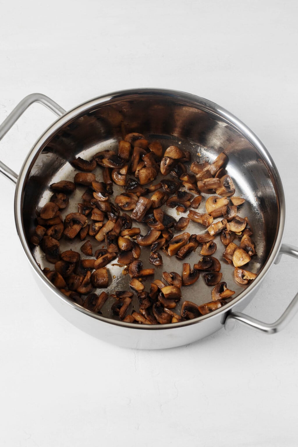 A large, silver pot holds mushrooms that are being sautéed.