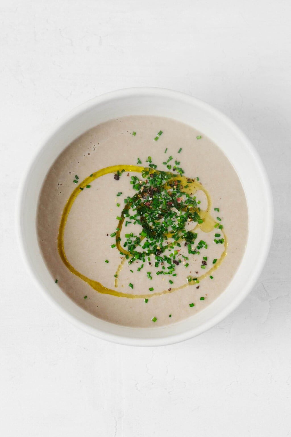 An overhead image of a round, white ceramic bowl that's holding pureed vegan cream of mushroom soup.